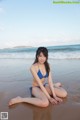 A woman in a blue bikini sitting on the beach.