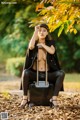 A woman sitting on top of a suitcase in a park.