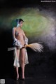 A naked woman holding a broom in front of a painting.