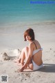 A woman in a white bikini sitting on the beach.