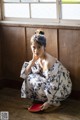 A woman in a kimono sitting on the floor next to a window.